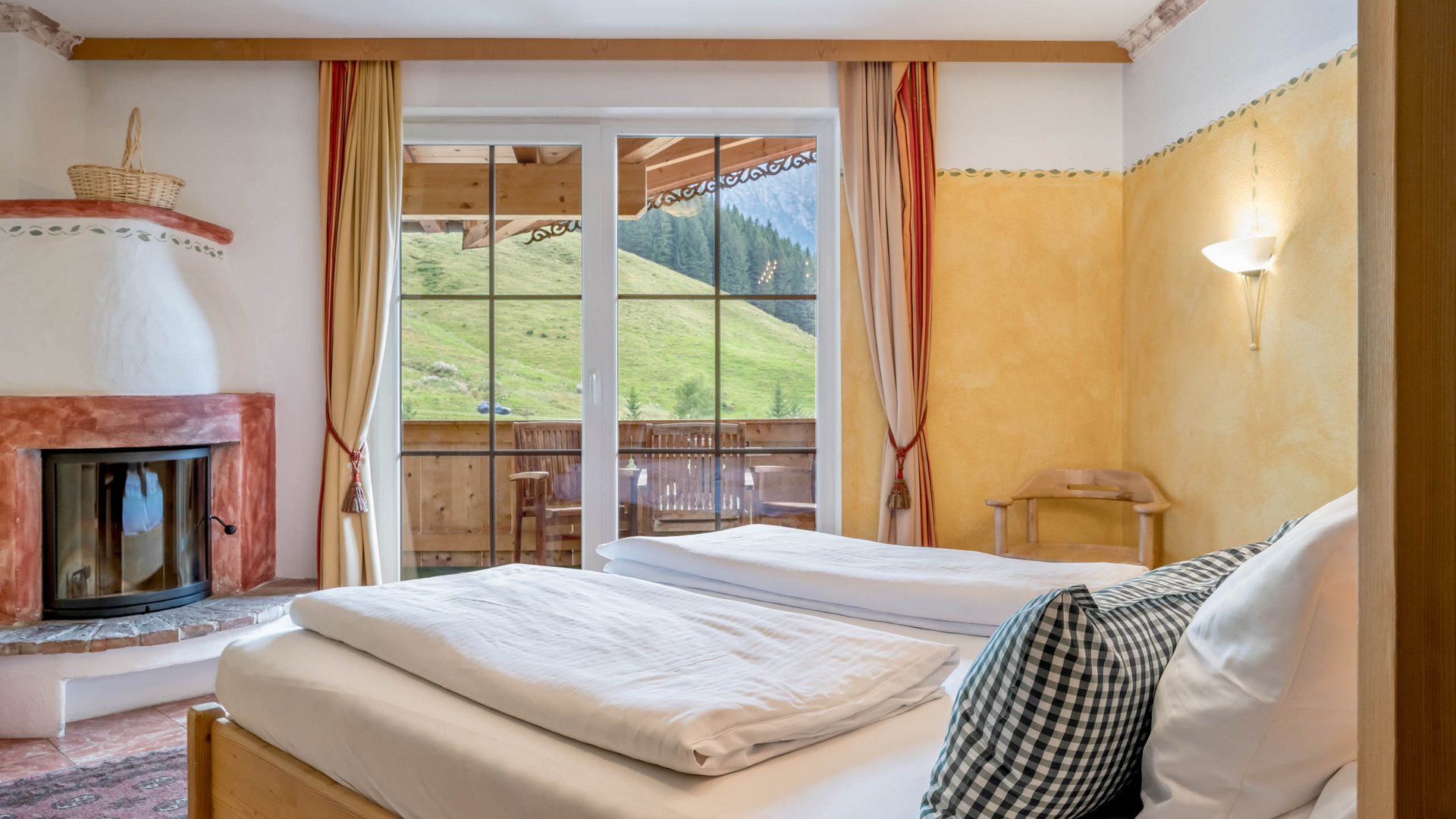 Rooms & suites in Gerlos • Der Grubacher: Eco Hotel in Tyrol Double bed in a hotel room with fireplace and balcony overlooking the mountainside