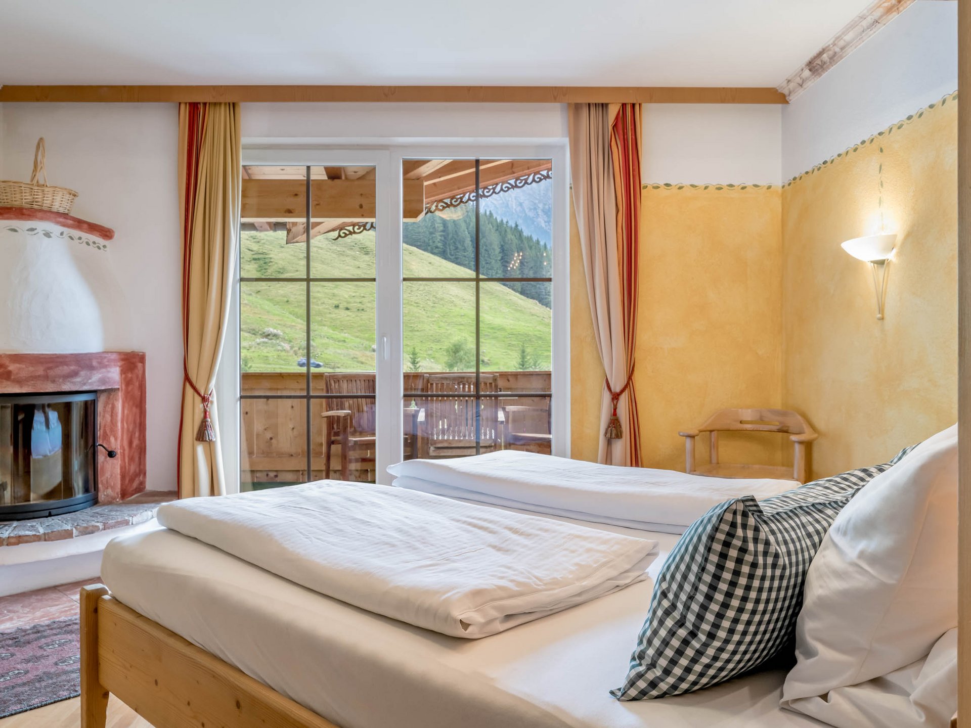 Der Grubacher • Biohotels in Gerlos im Zillertal in Tirol Doppelbett in einem Hotelzimmer mit Kamin und Balkon mit Blick auf den Berghang