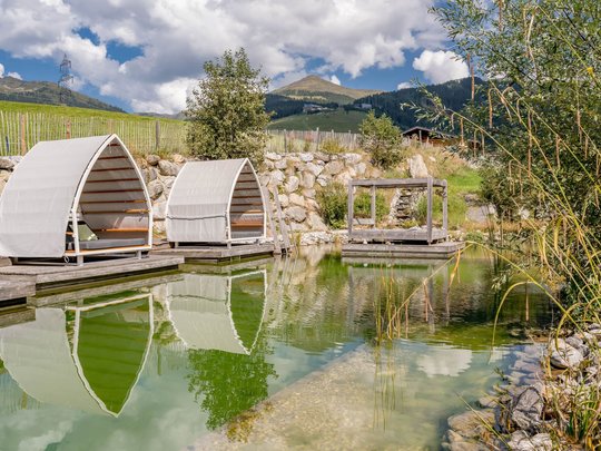 Our water world in Gerlos • Der Grubacher: Eco Hotel in Tyrol Swimming pond in the garden with a sun lounger and a view of the mountains