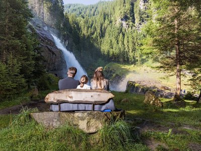 Around Gerlos • Der Grubacher: Eco Hotel in Gerlos Family on a bench in the forest overlooking the waterfall