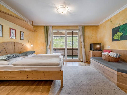 Rooms & suites in Gerlos • Der Grubacher: Eco Hotel in Tyrol Hotel room with double bed, TV, bench, and balcony overlooking the meadow