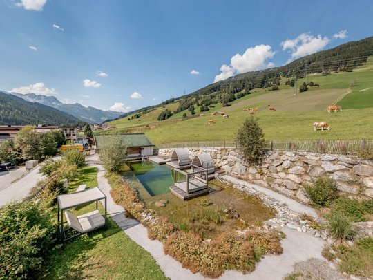 Our water world in Gerlos • Der Grubacher: Eco Hotel in Tyrol Garden with swimming pond, lounging areas, and view of the cow pasture