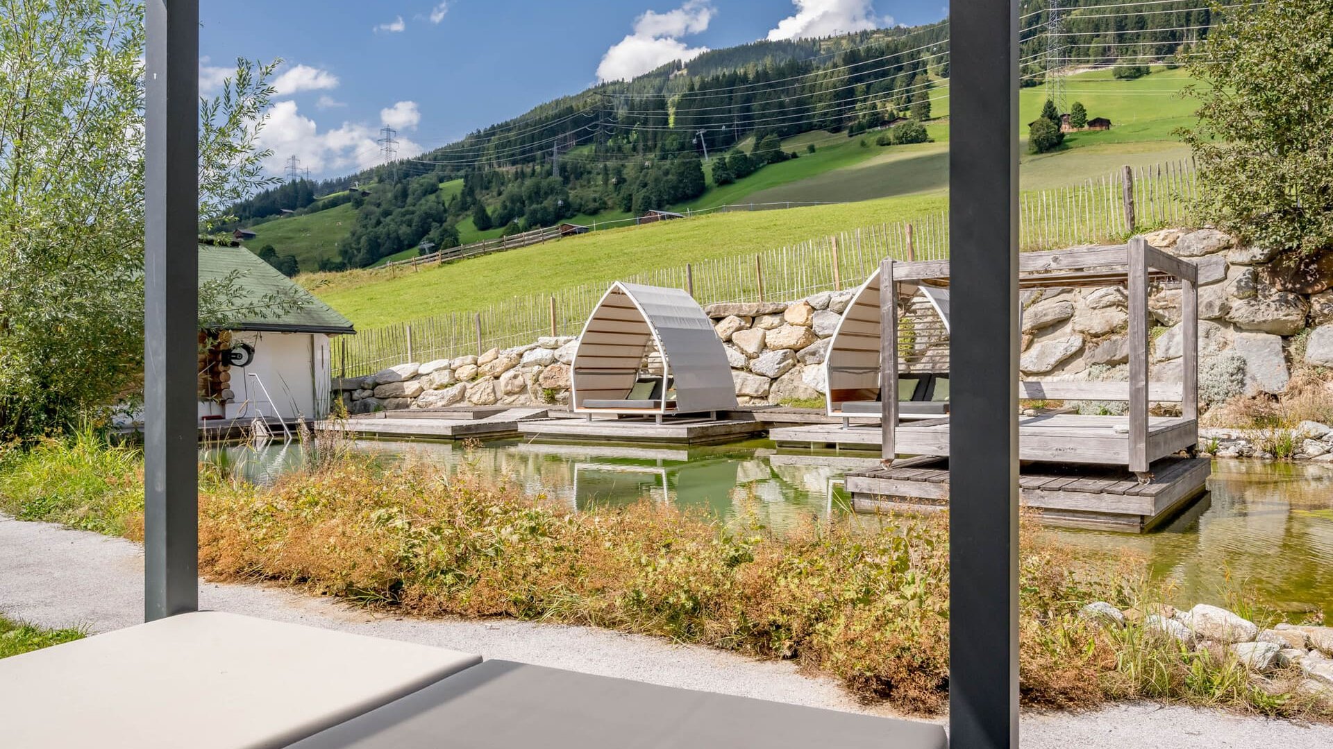 Our water world in Gerlos • Der Grubacher: Eco Hotel in Tyrol Swimming pond in the garden with lounging areas and view of the pasture