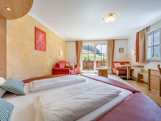 Rooms & suites in Gerlos • Der Grubacher: Eco Hotel in Tyrol Hotel room with double bed, sofa, and balcony overlooking the hillside